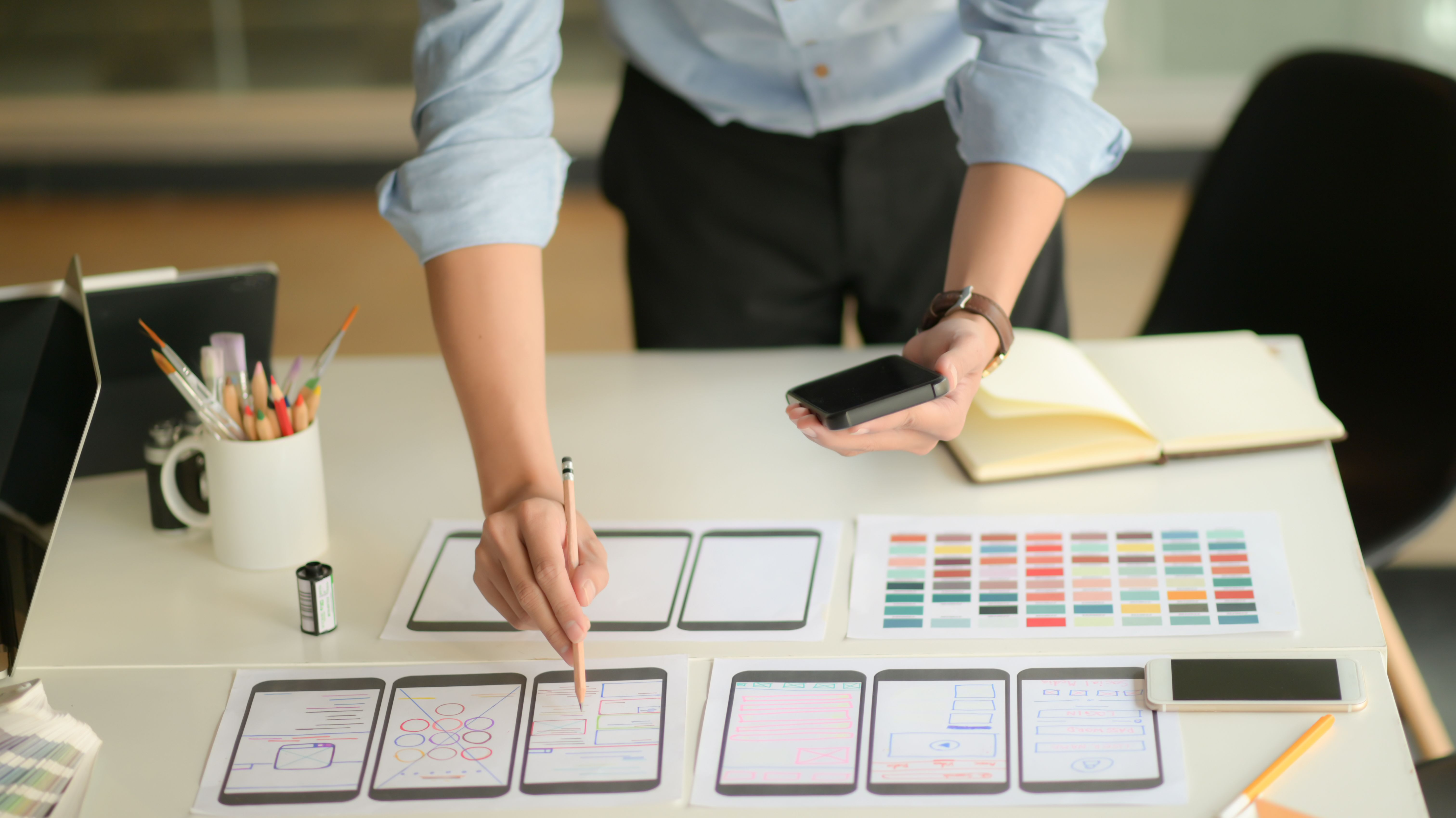 Designer with phone and pencil in hand creates mobile app design