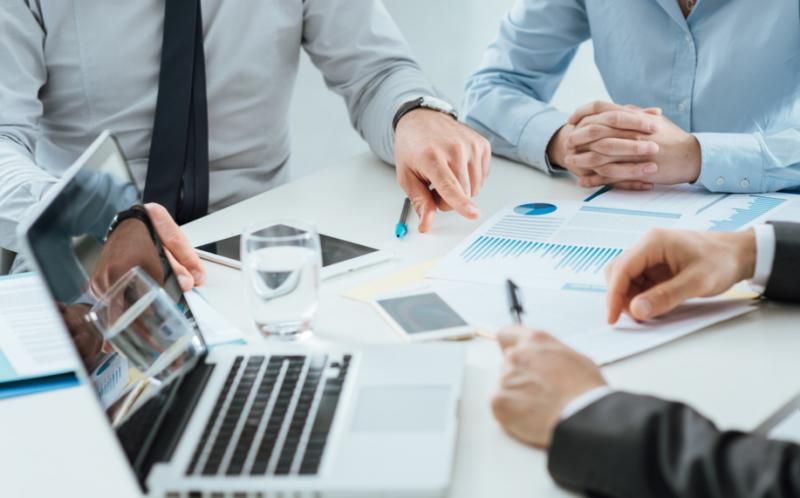 Arms and torsos of people in business shirts holding a meeting at their desk with a laptop and business papers to hire developers